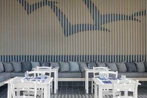 Restaurantbereich im Atlantica Kalliston Resort mit weißen Tischen und Stühlen, grauen Kissen und blauen Wanddekorationen.