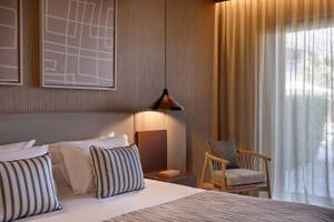 Ein elegantes Hotelzimmer mit Doppelbett, Kissen, Nachttisch und hängender Lampe im Atlantica Kalliston Resort.