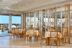Innenbereich des Astir Beach Hotels in Kreta mit geräumigen Tischen und Stühlen, Glaswänden und Aussicht auf den Pool.