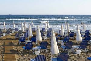 Strand des Astir Beach Hotels in Kreta mit vielen blauen Liegen und Sonnenschirmen.
