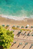 Luftaufnahme des Candia Park Village Strandes mit grünen Liegen und weißen Sonnenschirmen.