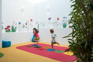 Kinder spielen auf einem roten Teppich mit nummerierten Quadraten in einem Zimmer mit Blumenwandgestaltung im Arminda Hotel & Spa.