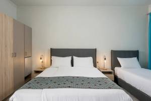 Zweibettzimmer im Corissia Beach Hotel mit zwei Betten, weißen Laken, Kopfkissen, Nachttischen und Lampen.