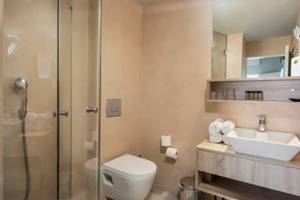 Badezimmer im Corissia Beach Hotel mit Glasdusche, Toilette, Waschbecken und Spiegel.