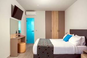 Innenansicht eines Zimmers im Corissia Beach Hotel mit einem Bett, einem Schreibtisch, einem Fernseher und einer Tür.