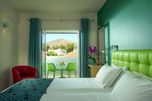 Zimmer im Corissia Beach Hotel mit grünem Bett, Balkon und Blick auf die Berge.