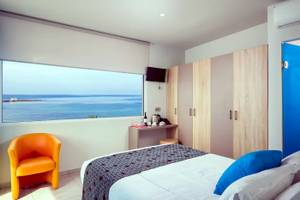 Zimmer im Corissia Beach Hotel mit Meerblick, Bett, oranger Stuhl, Fenster und Fernseher.