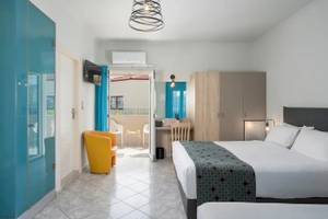 Innenansicht eines Zimmers im Corissia Beach Hotel mit zwei Betten, einem Schreibtisch, einer Klimaanlage und einem Balkon.