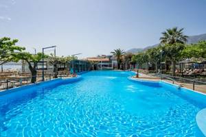 Ein großer blauer Swimmingpool im Corissia Beach Hotel mit umliegenden Bäumen und Bergen.