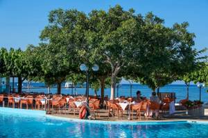 Außenterrasse am Pool des Corissia Beach Hotels mit orangefarbenen Stühlen und Tischen.