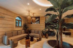 Loungebereich im Eliros Mare Hotel mit beigefarbenen Sofas, Holztischen, Pflanzen und Kronleuchtern.