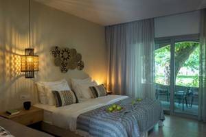 Schlafzimmer im Eliros Mare Hotel mit zwei Betten, Kissen, Bettwäsche, Lampen und offenem Balkon.