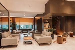 Innenansicht der Lobby des Eliros Mare Hotels mit modernen Möbeln, großen Fenstern und Pflanzen.