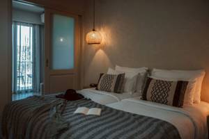 Doppelbettzimmer im Eliros Mare Hotel mit Bettwäsche, Kissen und einem offenen Buch auf der Bettdecke.