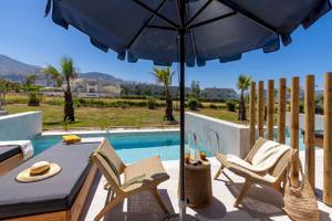 Außenbereich des Eliros Mare Hotels mit Pool, Liegen, Tisch und Sonnenschirm.