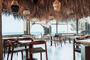 Innenansicht des Eliros Mare Hotels mit Blick auf das Meer, Tische und Stühle im Freien.