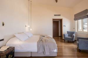 Schlafzimmer im Cretan Dream Resort & Spa mit großem Bett, Sesseln, Deckenventilator und Fenstern.