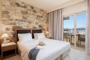 Ein Schlafzimmer im Cretan Dream Resort & Spa Hotel mit einem Bett, Steinwand, Balkon und Meerblick.