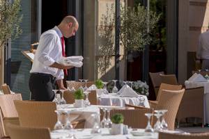 Ein Mann bereitet im Freien die Tische im Restaurant vor, wo mehrere Pflanzen und Gläser stehen.
