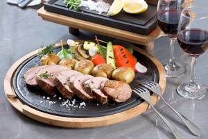 Fleischplatte mit Gemüse und zwei Weingläsern auf einem schwarzen Teller