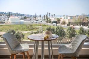 Zwei Stühle auf einem Balkon mit Aussicht auf eine Stadt, inklusive Tisch mit Flasche und Früchten.