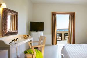 Innenansicht eines Hotelzimmers im Grecotel Meli Palace mit Bett, Schreibtisch und Balkon.