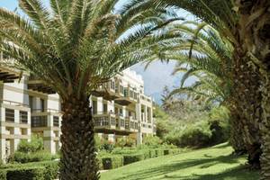 Das Grecotel Meli Palace Hotel mit Palmen und gepflegtem Rasen im Vordergrund.
