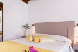 Schlafzimmer im Chrissi Amoudia Hotel mit weißen Wänden, gelben und weißen Kissen, und Blumen auf dem Bett.