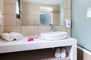 Badezimmer im Chrissi Amoudia Hotel mit Waschbecken, Spiegel und Handtüchern.