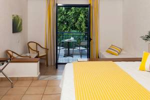 Hotelzimmer von Chrissi Amoudia mit Balkon, Bett, Tisch, Stühlen und Blick auf Bäume.
