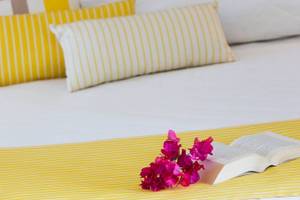 Foto von einem Bett im Chrissi Amoudia Hotel mit gelben Kissen und einer offenen Buch mit Blumen darauf.
