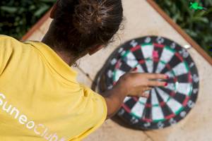 Eine Frau in einem gelben Suneo-Club-T-Shirt spielt Dart im Freien beim Chrissi-Amouida-Hotel.