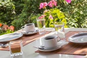 Frühstückstisch im Garten des Chrissi Amoudia Hotels mit Kaffee, Wasser und Gebäck.