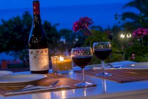 Romantisches Dinner im Hotel Chrissi Amoudia mit Weinflasche, Kerzen und Gläsern auf einer Tischplatte.