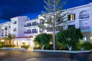 Die Außenansicht des Chrissi Amoudia Hotels bei Nacht mit einem großen Baum vor dem Gebäude.