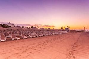 Strand mit Sonnenliegen und Sonnenschirmen vor dem Melas Lara Hotel bei Sonnenuntergang.