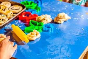Kinder backen Kekse mit Ausstechern und einer Walze auf einem blauen Tisch.
