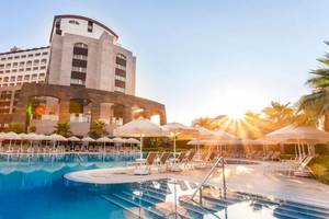 Melas Lara Hotel im Sonnenaufgang mit Swimmingpool und Sonnenschirmen.