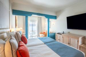 Innenansicht eines Doppelzimmers im LIVVO Volcan Lanzarote Hotel mit zwei Betten, Fernseher, Schränken und einer Veranda.