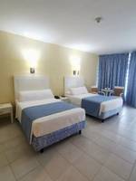 Zwei Doppelbetten im Zimmer des Muthu Playa Varadero Hotels, jedes mit weißen und blauen Laken, Nachttischen und Lampen an der Wand.