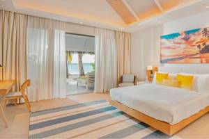 Eine Suite im Nova Maldives Hotel mit Blick auf das Meer, einem großen Bett, einem Tisch und einem Sessel.