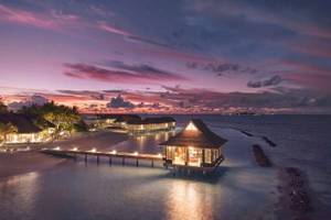 Nova Maldives Hotel bei Sonnenuntergang mit Blick auf das Meer und mehrere Wasservillen