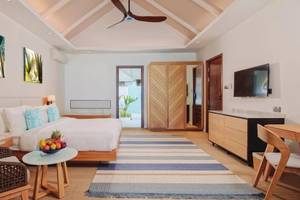 Innenansicht der Nova Maldives Suite mit großem Bett, Früchtetablett, Holzmöbeln und Fernseher.
