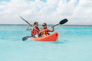 Zwei Personen paddeln in einem orangefarbenen Kajak auf dem Meer.