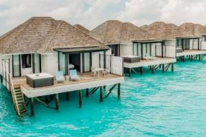 Reihe von Wasservillen im Nova Maldives Hotel mit blauem Wasser und blauem Himmel.
