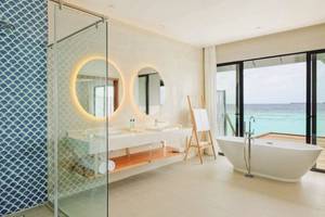 Badezimmer im Nova Maldives Hotel mit Meerblick, Badewanne, zwei Waschbecken und einer Dusche.