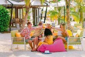 Gäste des Nova Maldives Hotels sitzen am Strand und chören mit Getränken in der Hand.