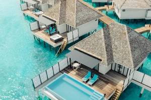 Aus der Luft aufgenommene Nova Maldives Wasservillen mit blauem Pool und Lounge-Bereich.