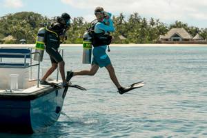 Scuba-Taucher betreten das Meer vor dem Nova Maldives Hotel.