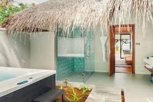 Außenbereich des Nova Maldives Hotels mit Jacuzzi und Duschbereich unter einem Strohhutdach.